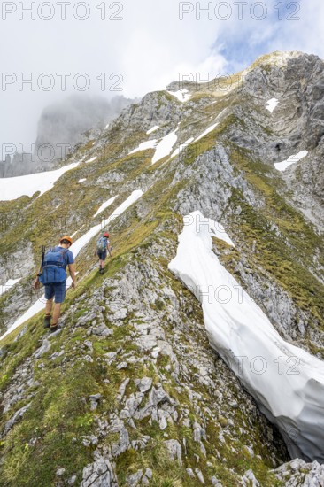 Two mountaineers with helmets on a narrow hiking trail, ascent to the Ackerlspitze, clouds moving around the mountains, Wilder Kaiser, Kaiser Mountains, Tyrol, Austria