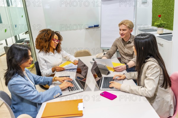 Four businesspeople using laptops and collaborating on a project in a modern coworking space, analyzing documents and discussing strategies
