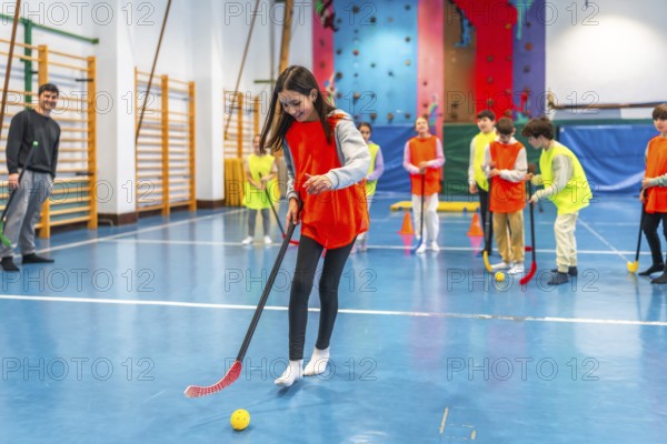 Elementary school students learning and playing floorball in a gym class with their teacher