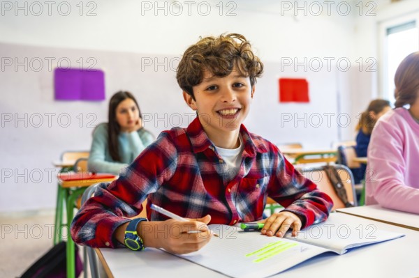 Happy elementary school student smiling and writing in notebook during class, with classmates in background