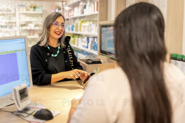 Woman using phone to show a product to a pharmacist standing in the counter of a pharmacy store