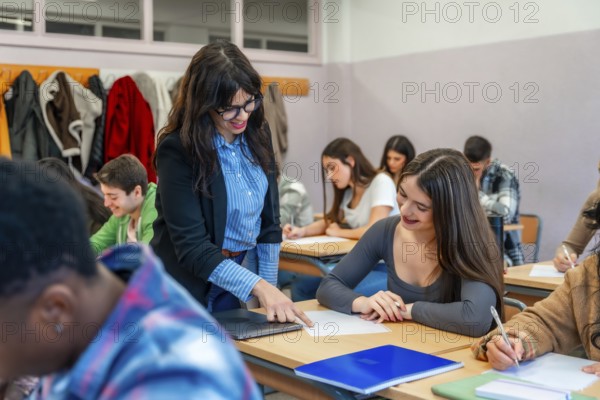 Female professor assisting a smiling student with her exam paper in a classroom full of diverse students taking a test