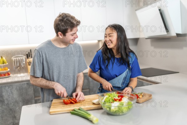 Asian woman and caucasian man enjoying quality time in a modern kitchen, chopping vegetables and making a fresh salad, promoting healthy living