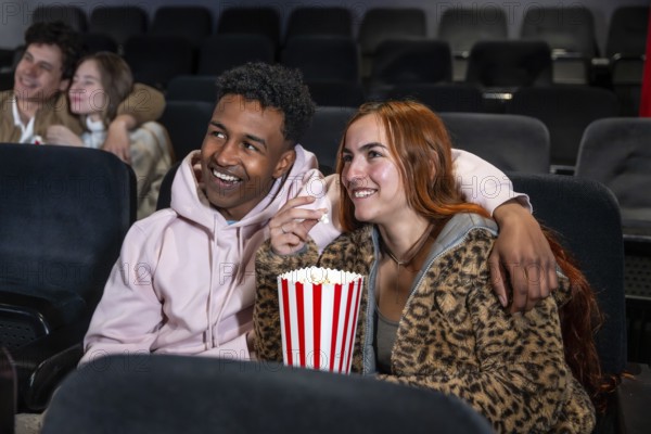 Happy couple sharing popcorn while watching a movie at the cinema, enjoying a night out with friends