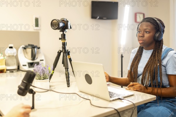 Young woman recording a vlog using a laptop, camera, microphone, and headphones in a home studio setting