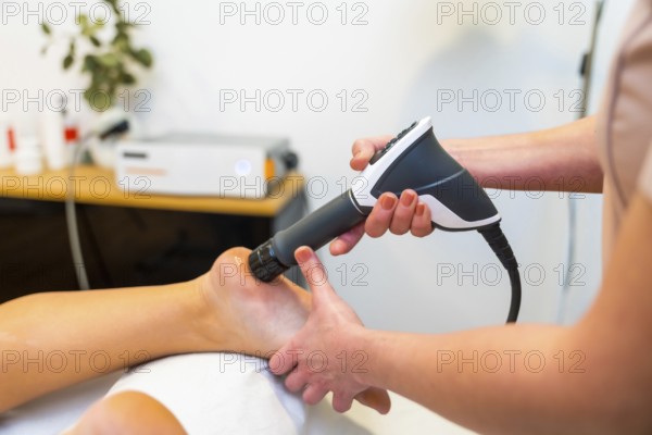 Close-up of an unrecognizable patient on stretcher receiving a shockwave therapy massage on foot in a holistic clinic