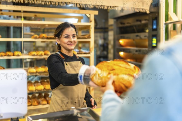 Latin smiling woman selling bread to a client in an artisan bakery