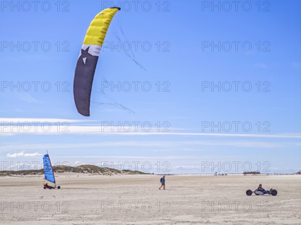 Recreational sport Beach kiting on the edge of the national park and UNESCO World Heritage Site, designated kite area, kite buggy steered with both feet, driver's seat with kiter between rear axle and front wheel, high speed, westerly winds, dunes on the beach, sunshine and blue sky, Sankt Peter-Ording, Schleswig-Holstein, Germany