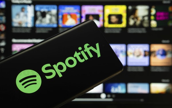 Dhaka, Bangladesh - 18 March 2025: The logo of the spotify is displayed on a smartphone screen, and the website spotify is visible on a computer screen in the background