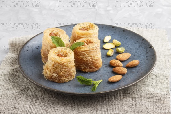 Kunafa, traditional arabic sweets in blue ceramic plate on a gray concrete background. side view, close up