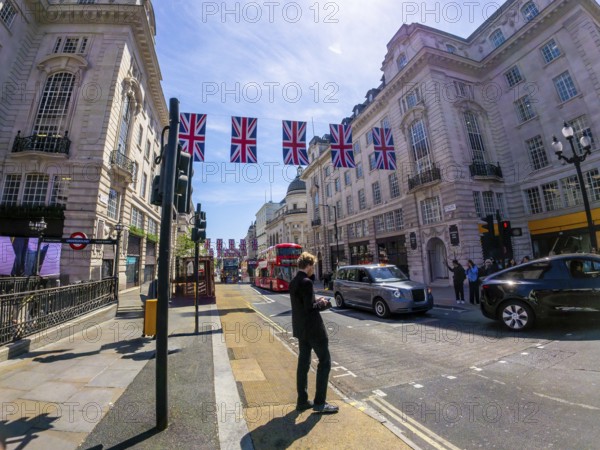 Businessman using smartphone on a london street decorated with british flags, with typical red bus and black cab in the background