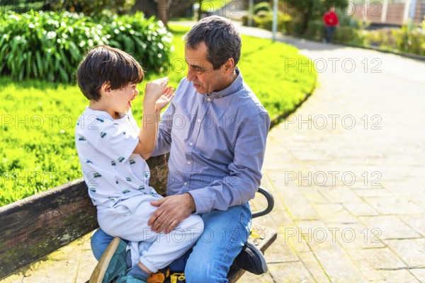 Grandfather and grandson enjoying a playful moment together, sitting on a park bench surrounded by greenery