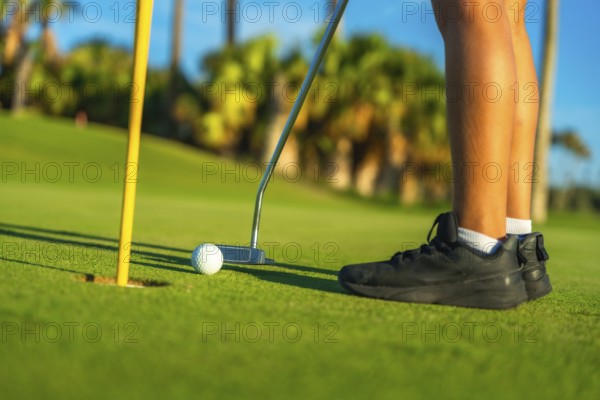 Person putting golf ball in a green course, low section