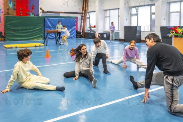 Group of smiling students practicing stretching exercises with their teacher during physical education class in a school gym