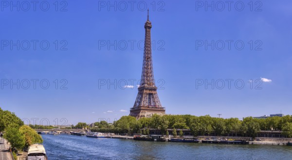 The Eiffel Tower from afar with a river and green treetops on a sunny day, Paris