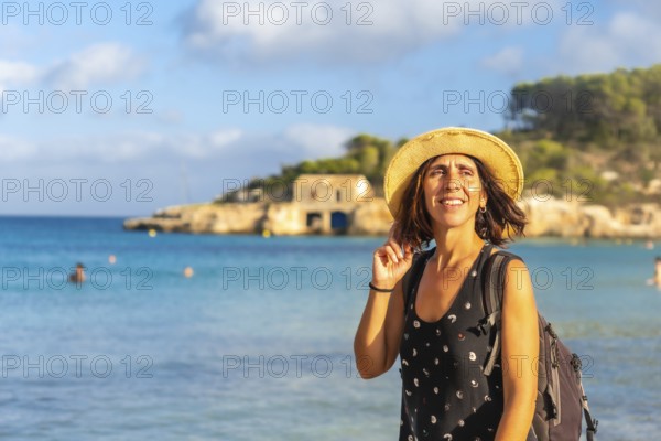 Female tourist with backpack and straw hat enjoying summer holidays on beautiful s'amarador beach in mallorca, spain