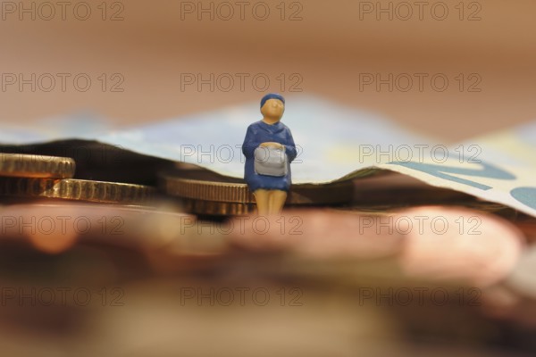 Miniature woman sitting on euro coin, twenty euro note in the background, North Rhine-Westphalia, Germany