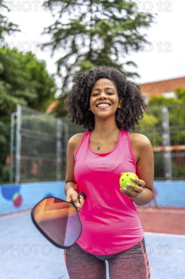 Vertical portrait of a latin female pickelball player standing smiling at camera in an outdoor court