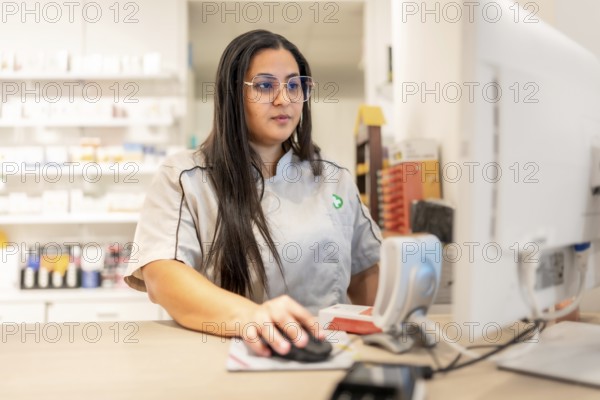 Young female pharmacist looking for a product in the inventory using computer