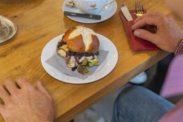 A burger on a pretzel bun is served on a table in the restaurant, autumn creations, Cafe Kuh, Deckenpfronn, Black Forest, Germany