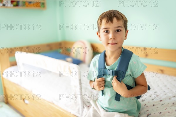 Portrait of a schoolboy with school bag ready for first day at school smiling at camera in the bedroom