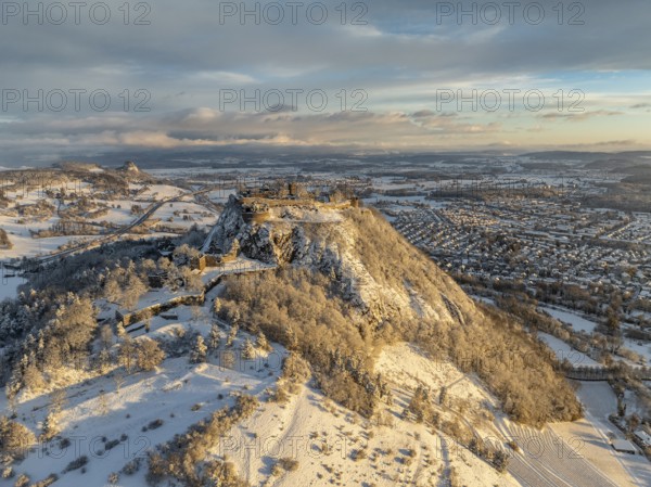Aerial view of the snow-covered Hegau volcano Hohentwiel with Germany's largest castle ruins on a cold winter morning, at sunrise, on the right the town of Singen, on the left on the horizon the neighbouring Hegau volcano Hohenkrähen, district of Constance, Baden-Württemberg, Germany
