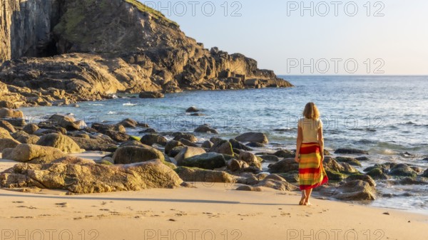 A woman on a sandy beach in Nanjizal Bay. Evening, golden hour. St Just, Penzance, Cornwall, England, Great Britain