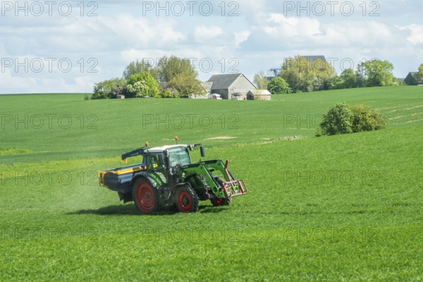 Tractor spreading fertilizer on a field with green crops in Sjörup, Ystad municipality, Skåne county, Sweden, Scandinavia