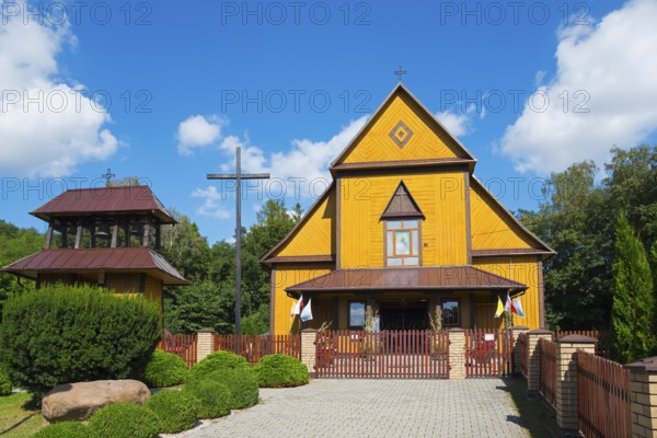 Yellow wooden church in summer under a blue sky with a wooden fence and surrounded by trees, Church of the Holy Apostles Peter and Paul, Olbiecin, Olbiecin, Powiat Krasnik, Krasnik, Lublin Voivodeship, Poland