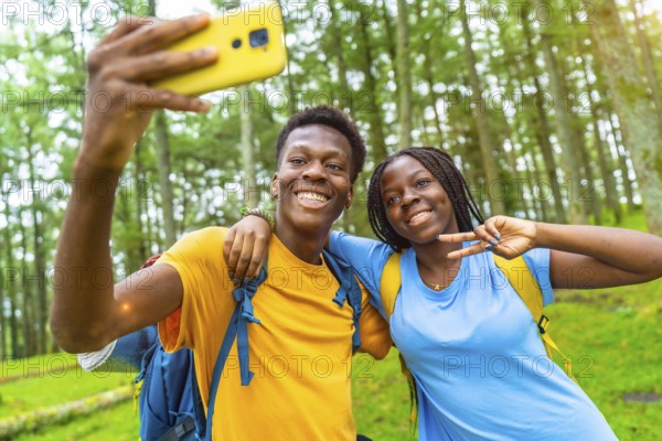 Cheerful african friends taking selfie gesturing victory with hand while hiking in the forest