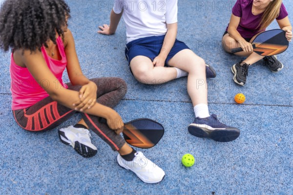 Latin woman and friends talking sitting on a pickelball court after playing together