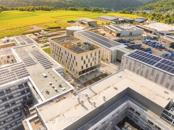 Building with solar panels on the roof, surrounded by fields and industrial plants, construction of the new hospital health campus Calw, Germany