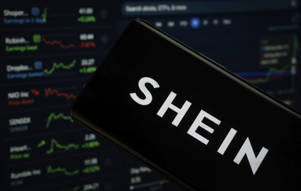 Dhaka, Bangladesh- 18 March 2025: shein logo is displayed on a smartphone screen, with a stock graph webpage visible on a computer screen in the background