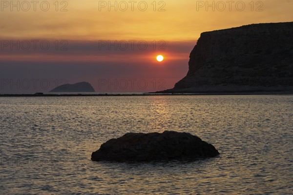 Sunset, sun next to cliff, rocks in the sea, Pontikos Island, orange sky, grey clouds, Gramvoussa Peninsula, Pirate Bay, Balos, Tigani, West Crete, Crete Island, Greece