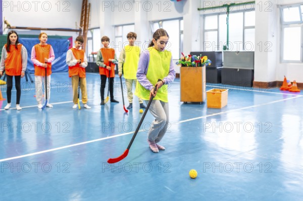 Group of elementary school students wearing vests practicing floorball in gym class, learning teamwork and hand eye coordination