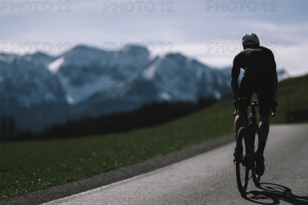 Road bike rider in spring near Halblech in the Allgäu in front of a picturesque backdrop of the Alps, Bavaria, Germany