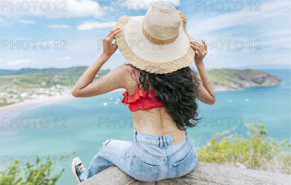 Rear view tourist girl sitting at a viewpoint looking at the beach. Back view of woman on vacation looking at the beach at a viewpoint