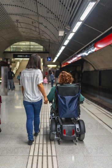 Rear view of a disabled woman and caregiver in the platform of the metro