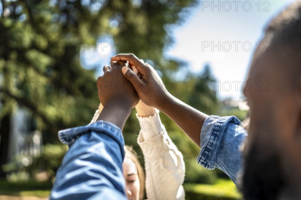 Multi-ethnic couple holding hands and raising them in a park