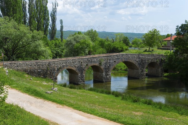 Stone bridge over a quiet river, surrounded by green nature under a blue sky, bridge over the river Zrmanja, Žegar, Zegar, Zadar, Croatia