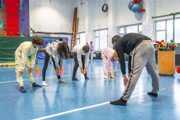 Teenagers bending forward and touching toes while exercising together in school gym class
