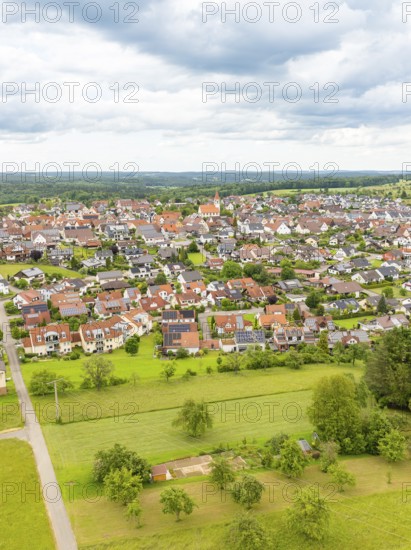Aerial view of a village with red roofs, surrounded by green meadows and trees under a cloudy sky, Deckenpfronn, Black Forest, Germany