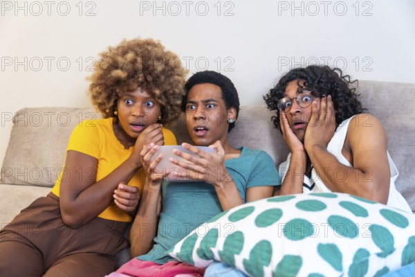 Multi-ethnic friends watching horror movie and eating pop corn sitting on the sofa at home