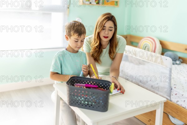 Mother and her son doing homework together and coloring on the bedroom