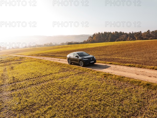 A black car on a dirt road in the middle of golden autumnal fields in sunlight, electric car VW ID5, Deer Carsharing, Gechingen, Black Forest, Germany