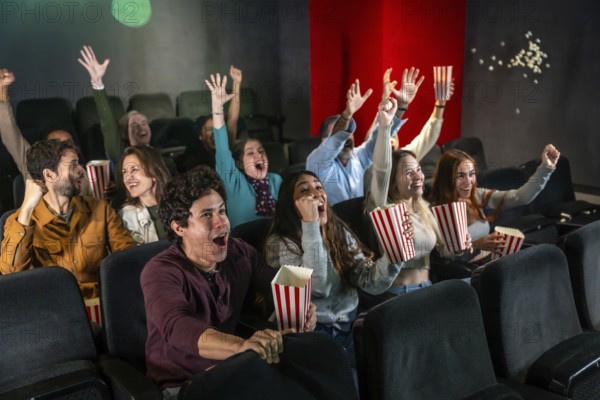 People enjoying a movie, raising hands and cheering while eating popcorn in a dark movie theater