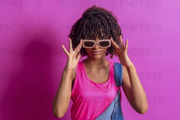 Fashionable young woman adjusting her sunglasses while posing against a vibrant pink backdrop