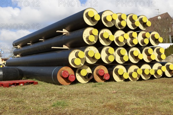 Stacked district heating pipes and district heating lines with yellow ends lie piled up in a meadow