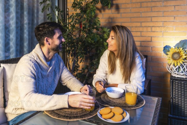 Smiling couple having breakfast together on their balcony, enjoying a peaceful moment with orange juice, cookies, and cereal