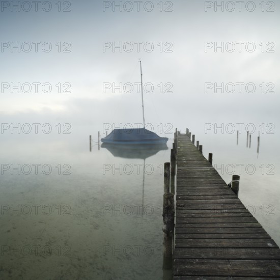 Quiet autumn morning on Lake Chiemsee, jetty with sailing boat in dense fog, Prien am Chiemsee, Bavaria, Germany